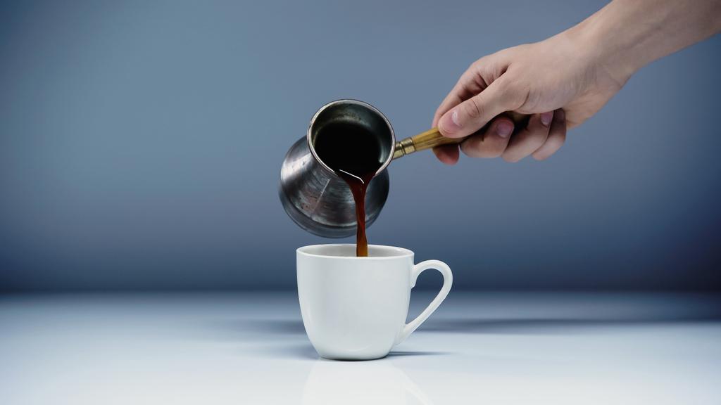 abgeschnittene Ansicht eines Mannes, der Kaffee in Tasse auf Weiß und Grau gießt  - Foto, Bild