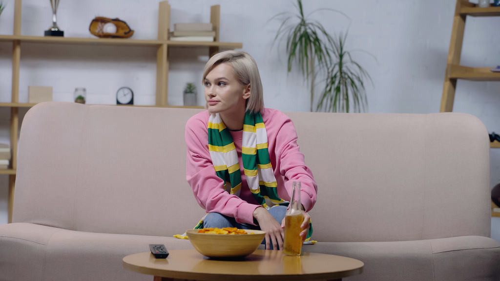 upset woman in striped scarf holding bottle of beer while watching sport championship at home - Foto, Imagem