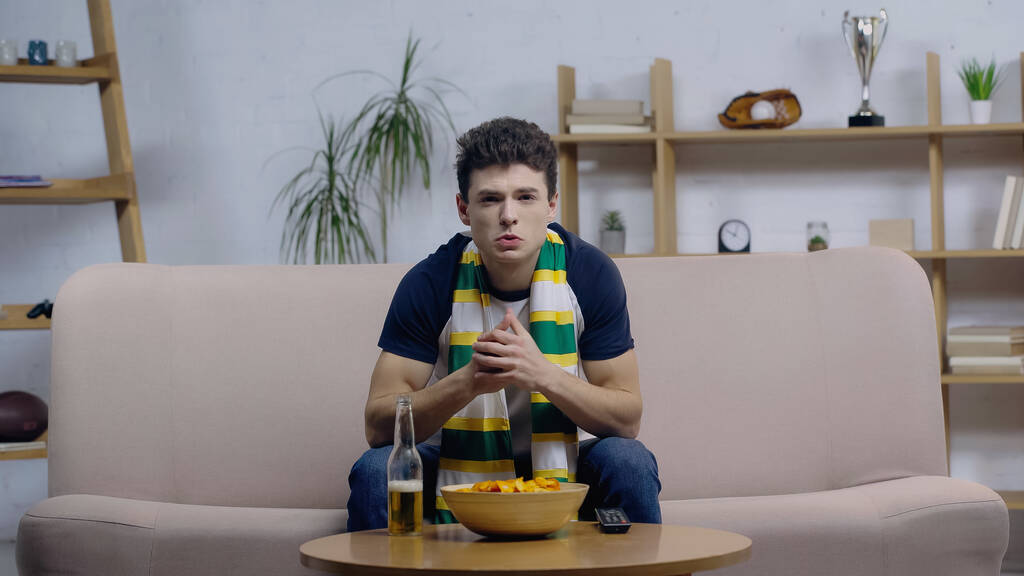 Besorgter junger Mann schaut Sportspiel zu Hause bei Bier und Chips im Fernsehen - Foto, Bild