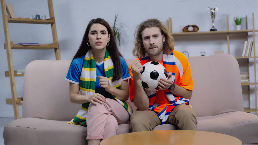 концентровані друзі в смугастих шарфах дивитися футбольний матч на телебаченні вдома
 - Фото, зображення