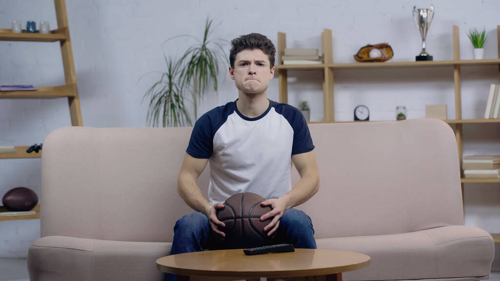 хвилюючий фанат баскетболу тримає м'яч під час перегляду матчу на телебаченні вдома
 - Фото, зображення