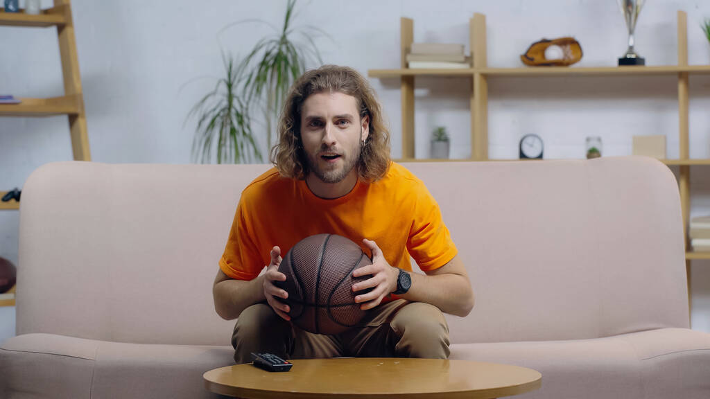 fã de esporte focado segurando bola enquanto assiste jogo de basquete em casa tv - Foto, Imagem
