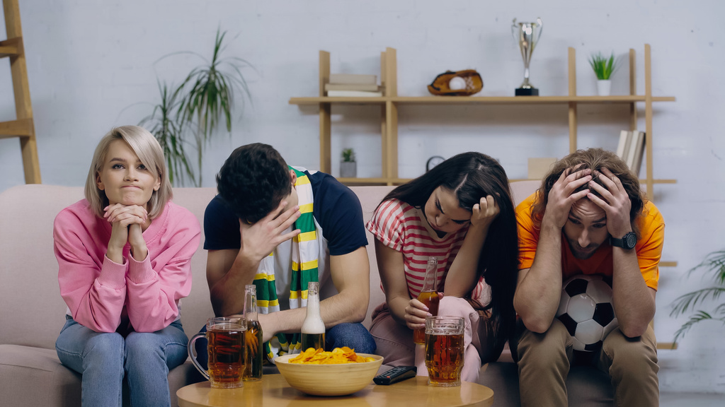 разочарованные футбольные болельщики сидят с склоненными головами возле пива и чипсов дома - Фото, изображение