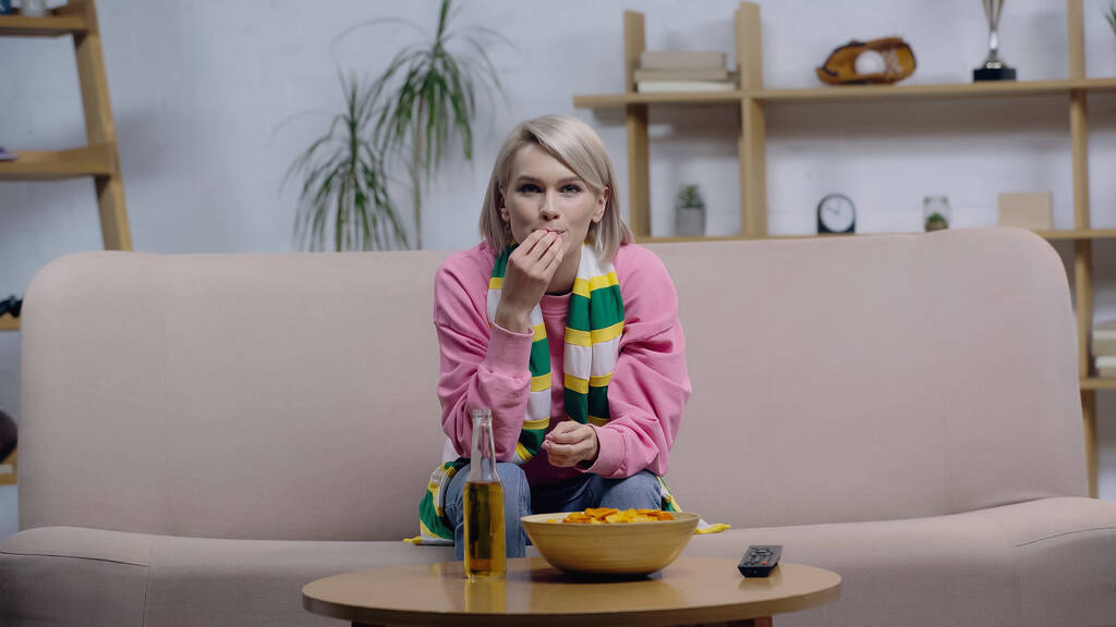 концентрована вентиляторна жінка їсть фішки під час перегляду гри на телебаченні вдома
 - Фото, зображення