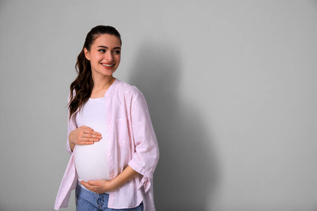 Giovane donna incinta su sfondo grigio chiaro. Spazio per testo - Foto, immagini