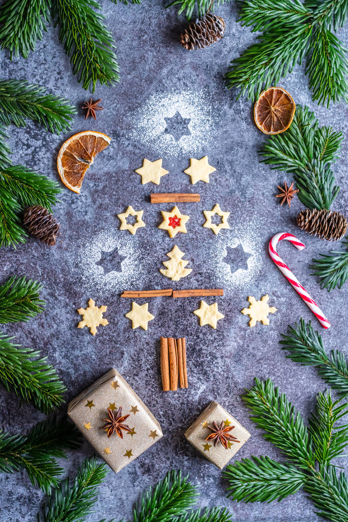 Noel tatlısı ve kurabiyeleri gri masaya kozalaklı ve dallı bir Noel ağacı şeklinde yerleştirilmiş. Kış ve Noel süslemeleri, tarçın, şeker ve yıldız anason. - Fotoğraf, Görsel