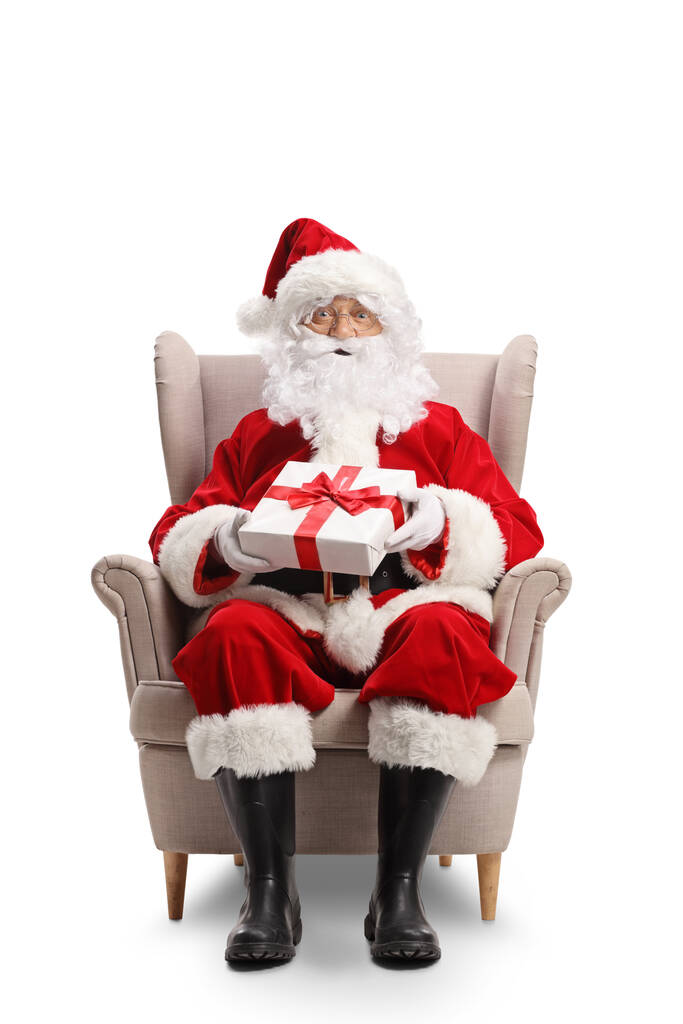 Portrait complet du Père Noël assis dans un fauteuil avec un cadeau dans ses mains isolé sur fond blanc - Photo, image