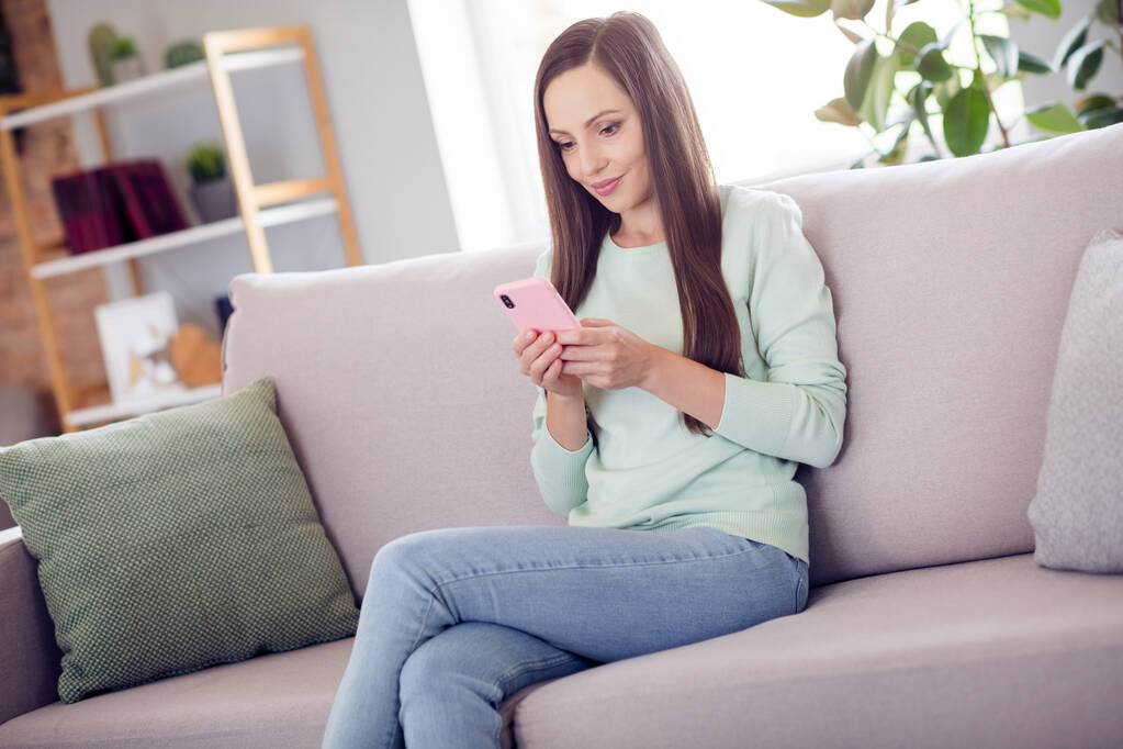 Fotografie roztomilé mladé brunetky dáma sedět na pohovce s telefonem nosit modré košile džíny doma sám - Fotografie, Obrázek