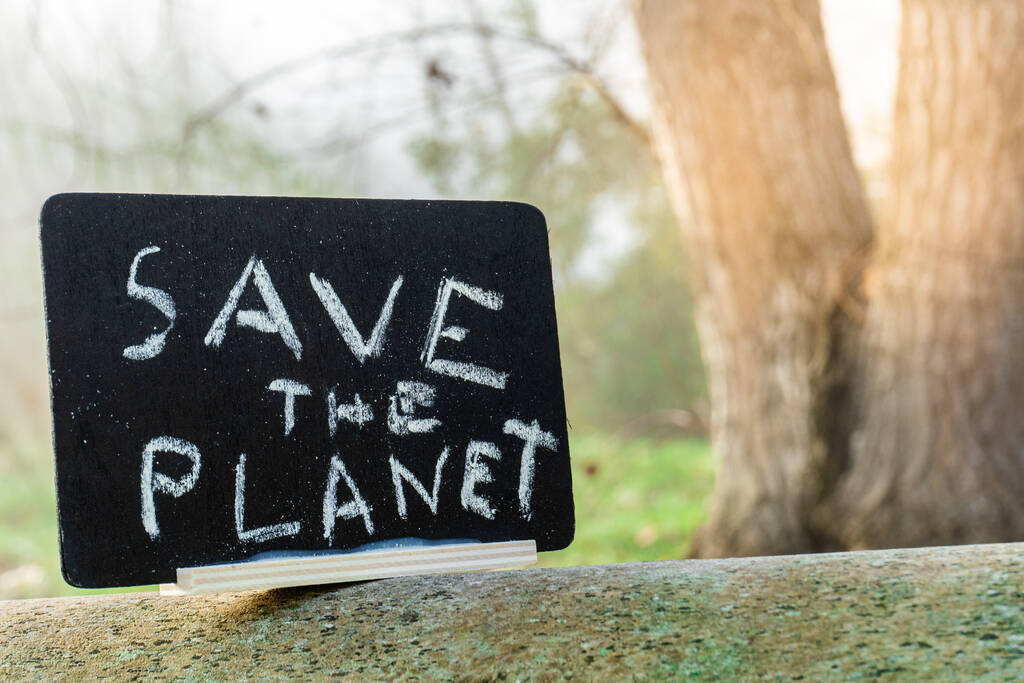 Η χάρτινη πινακίδα με το σύνθημα Σώστε τον Πλανήτη στο δέντρο με το θολό φόντο - Φωτογραφία, εικόνα