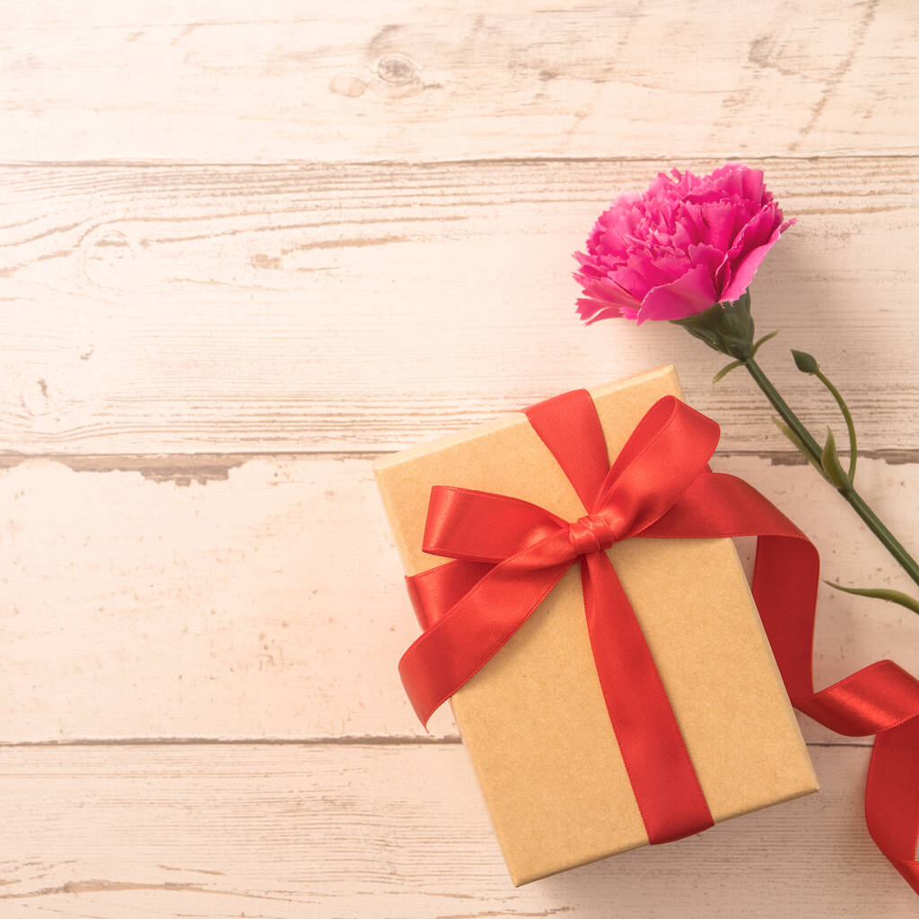 Крафт подарочная коробка с красной лентой лук и гвоздика, концепция дарения подарок на День матери, как сюрприз, плоский лежал, вид сверху - Фото, изображение
