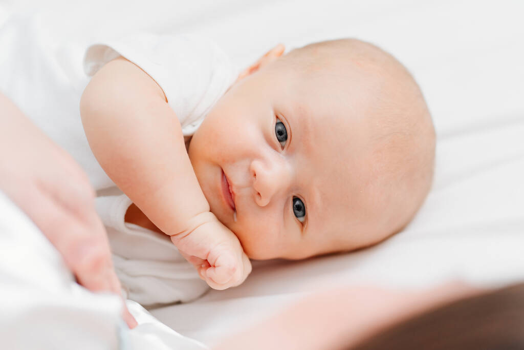 un lindo bebé con una gota de leche en la esquina de la boca en la cama cerca de la madre. - Foto, Imagen