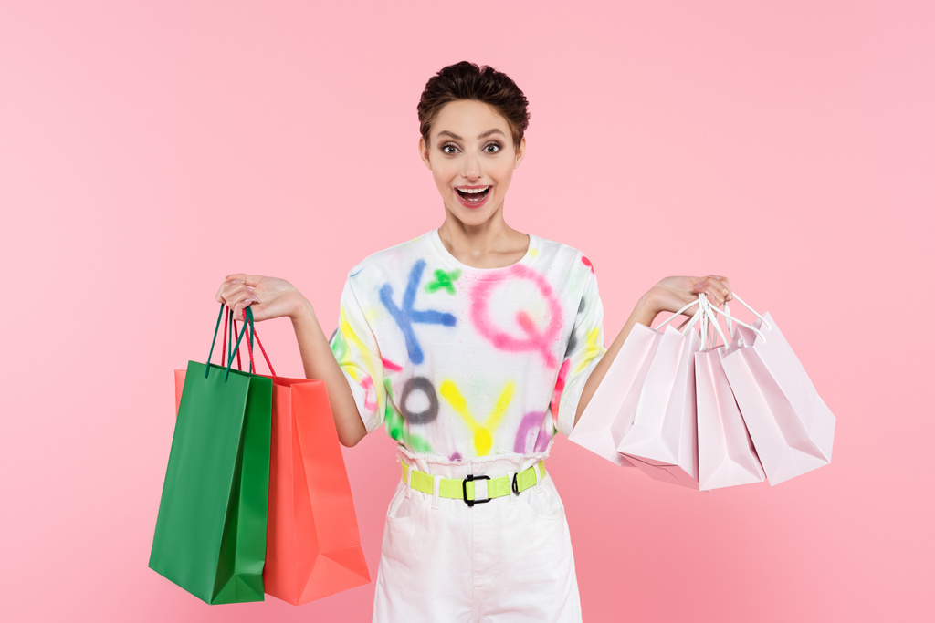 Heyecanlı ve şık bir kadın, elinde pembe renkli alışveriş torbalarıyla kameraya bakıyor. - Fotoğraf, Görsel
