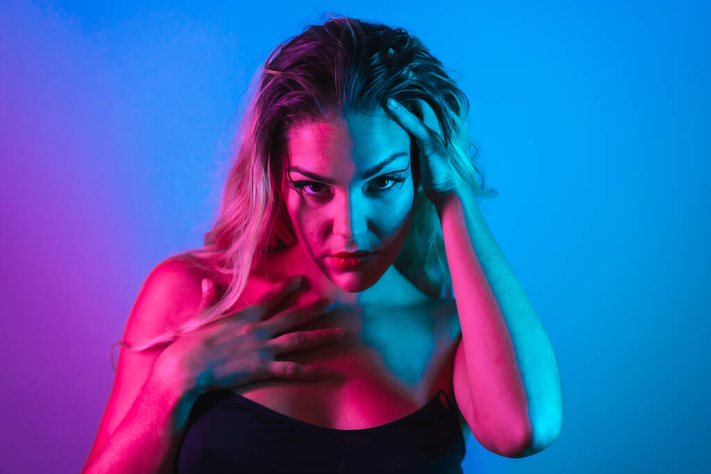 A Caucasian blonde girl in a black t-shirt with eye drawing makeup, eyelashes arranged on a blue background with pink neon lights - Fotoğraf, Görsel