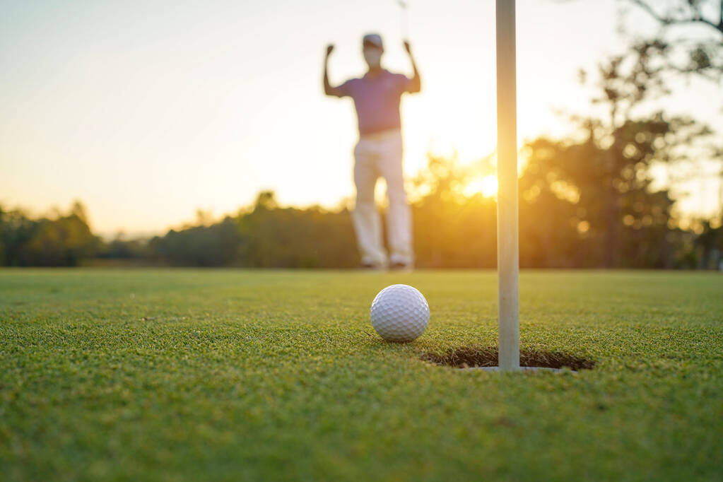 Golfer zet bal op de groene golf, lens flare op zonsondergang 's avonds tijd. Golfer actie te winnen na lange putting golfbal in het gat.                                 - Foto, afbeelding