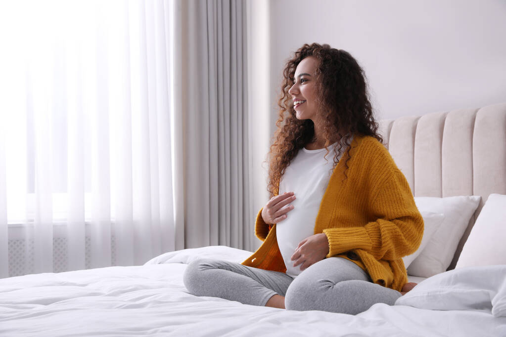 Embarazada joven afroamericana sentada en la cama en casa - Foto, Imagen