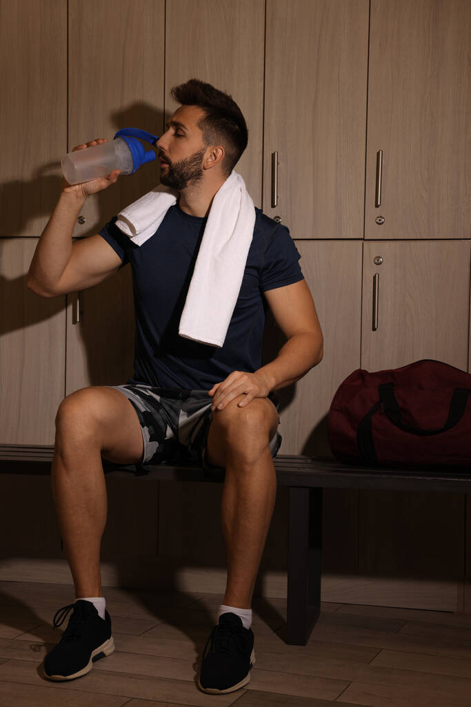 Handsome man drinking water in locker room - Photo, Image