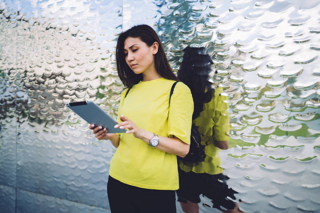 Pensive ασιατική γυναίκα σε casual φορούν στέκεται σε εξωτερικούς χώρους ανάγνωση ειδήσεων και κοινοποίηση σε ψηφιακή ταμπλέτα, σοβαρή influencer hipster κορίτσι 20 βλέποντας βίντεο μέσω touchpad και 4G σύνδεση στο internet - Φωτογραφία, εικόνα