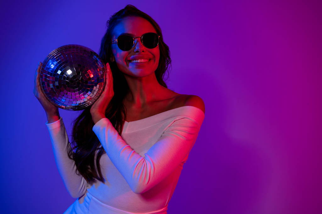 Fénykép édes Y-generációs barna hölgy disco labda visel fehér felső szemüveg elszigetelt felett gradiens színes háttér - Fotó, kép