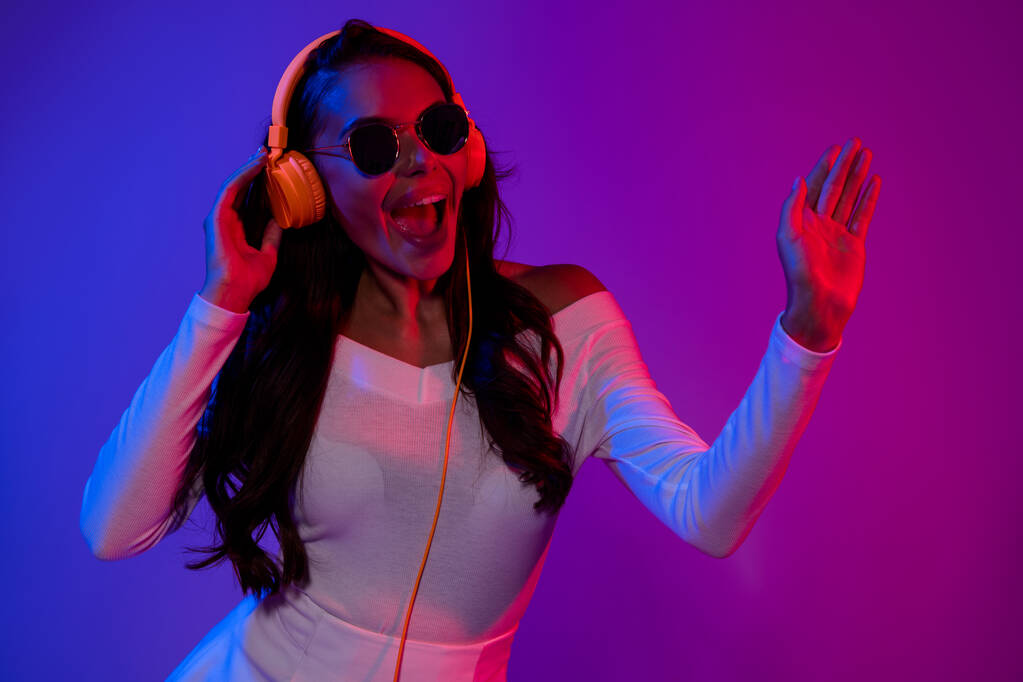 Foto de divertida dama morena hipster millennial escuchar música danza con gafas vestido blanco aislado sobre fondo colorido gradiente - Foto, imagen