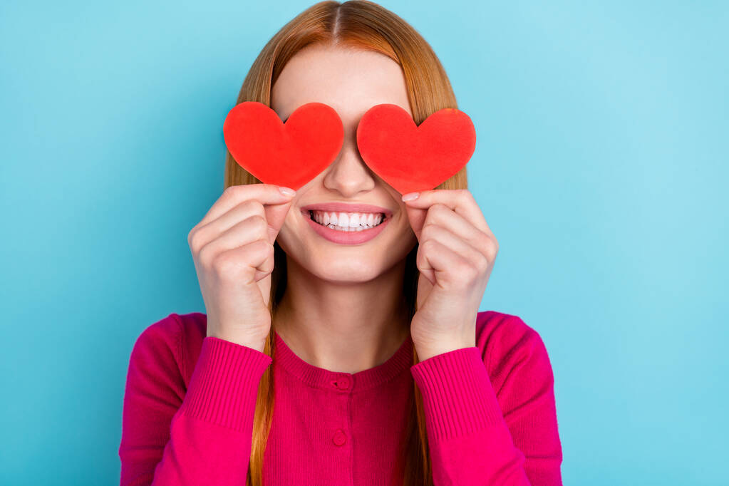 Foto de mujer joven brillante funky usar camisa rosa dos corazones rojos cubren los ojos sonriendo aislado fondo de color azul - Foto, imagen