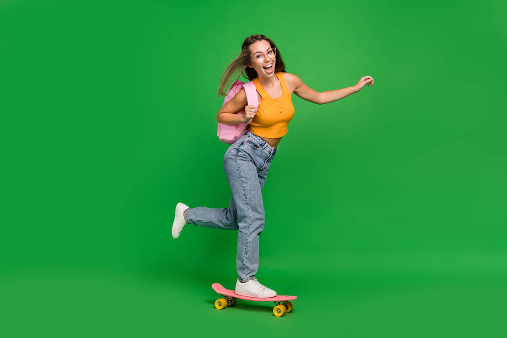 Full length photo of millennial impressed brunette lady skater wear top jeans shoes bag eyewear isolated on green background - Foto, Imagem