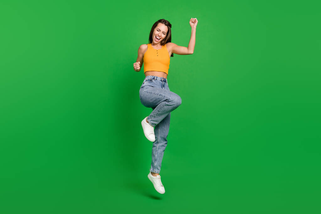 Full size photo of young hooray brunette lady jump wear top jeans shoes isolated on green background - Foto, Bild