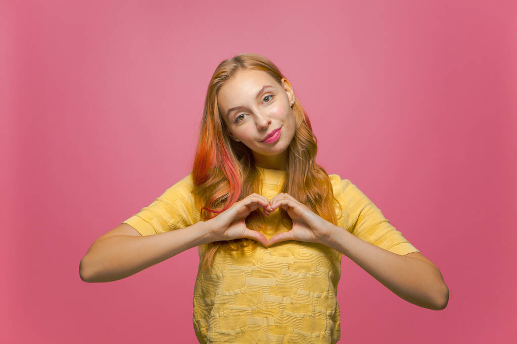Pretty young girl show heart gesture with love, feeling romantic mood, sympathy, support on pink studio background - Foto, immagini