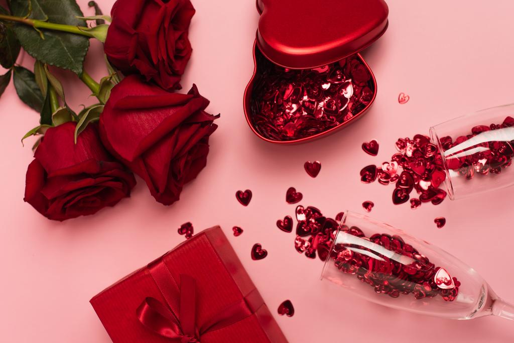 κορυφαία άποψη των ποτηριών σαμπάνιας με καρδιές κομφετί κοντά κουτιά δώρων και τριαντάφυλλα σε ροζ - Φωτογραφία, εικόνα