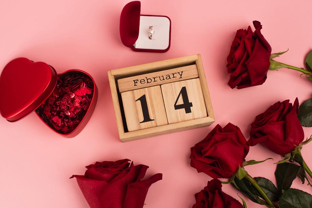 top view of red roses near calendar with 14 february lettering, confetti and engagement ring on pink  - Photo, Image