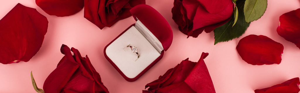 плоская укладка красных лепестков роз вокруг ювелирной коробки с бриллиантовым кольцом на розовом, баннер - Фото, изображение