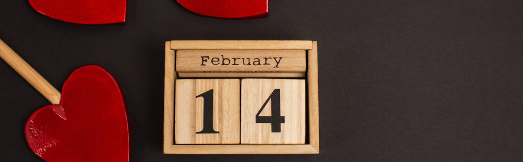 top view of wooden calendar with 14 february lettering near heart-shaped lollipops on black, banner - Foto, Bild