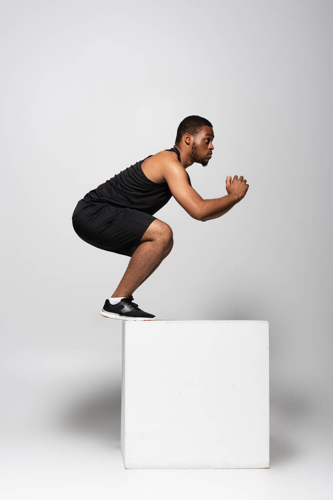 full length of african american sportsman jumping on white cube on grey - Photo, Image