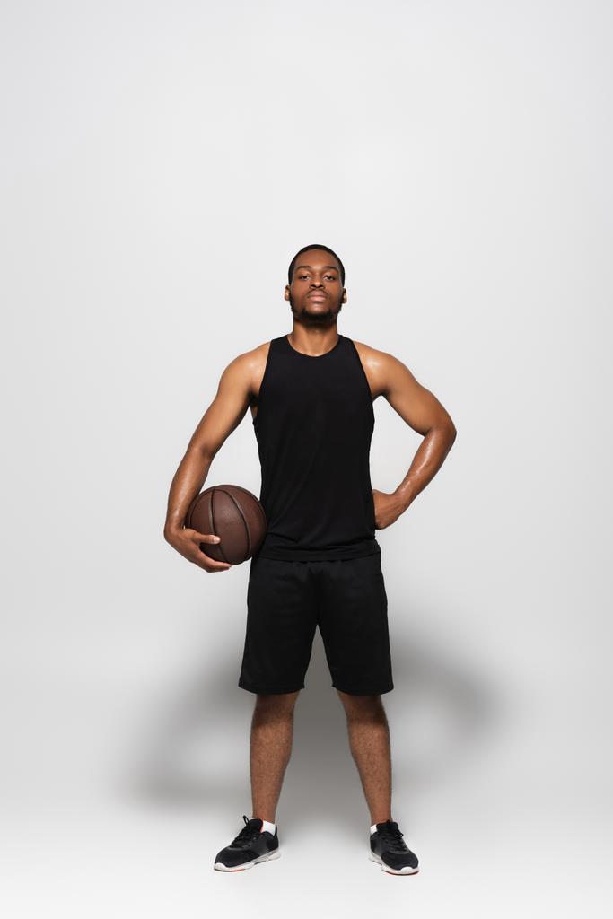 アフリカ系アメリカ人選手がバスケットボールをしながら腰を上げてグレーで立っています - 写真・画像