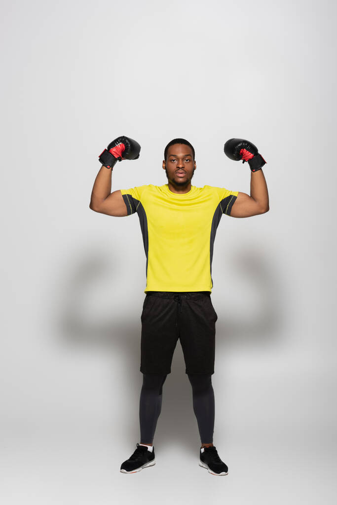 полная длина мускулистого африканского спортсмена в боксёрских перчатках на сером - Фото, изображение