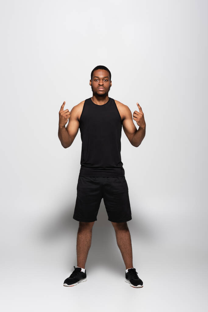longitud completa del deportista afroamericano en camiseta sin mangas y pantalones cortos que muestran un cartel de roca en gris - Foto, imagen