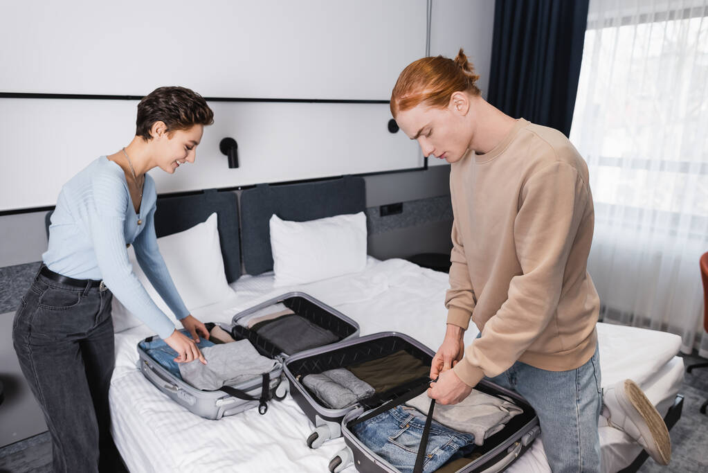 Вид збоку усміхнена пара розпаковує валізи в готельному номері
  - Фото, зображення