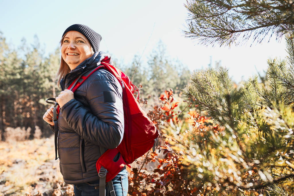 Femme souriante profitant d'une randonnée le jour de vacances ensoleillé. Femme avec sac à dos marchant dans la forêt. Passer des vacances d'été près de la nature - Photo, image