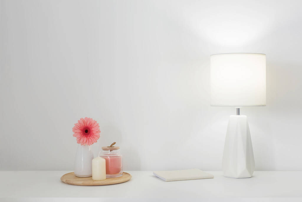 pink gerber in vase, candles and modern lamp on white shelf - Foto, Bild