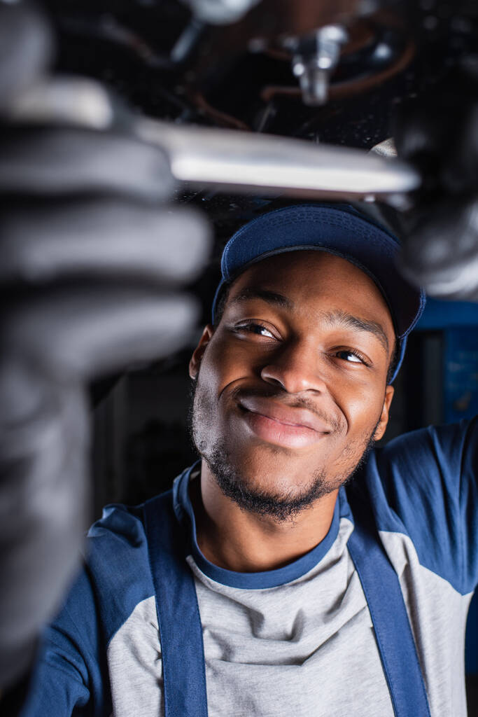 奉仕中の車の下で働くアフリカ系アメリカ人のフォアマンの笑顔  - 写真・画像