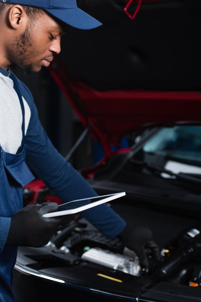 young african american repairman holding digital tablet while making inspection of blurred car - Foto, Bild