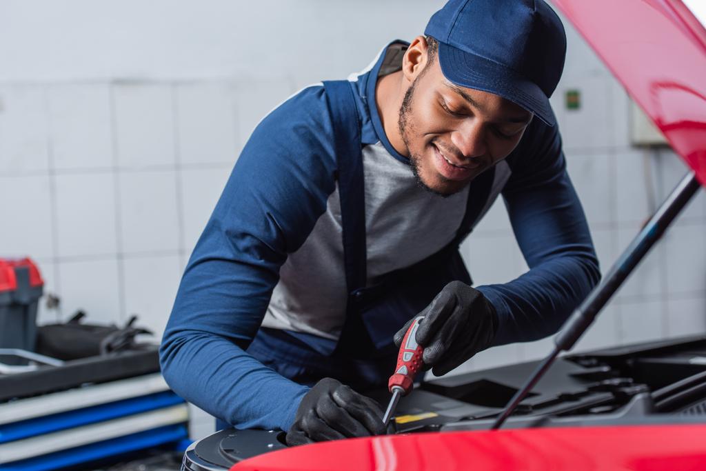 smiling african american foreman making diagnostics of blurred car in workshop - Photo, Image