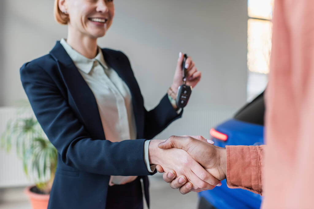 partial view of car dealer holding key while shaking hands with blurred african american client - Фото, изображение