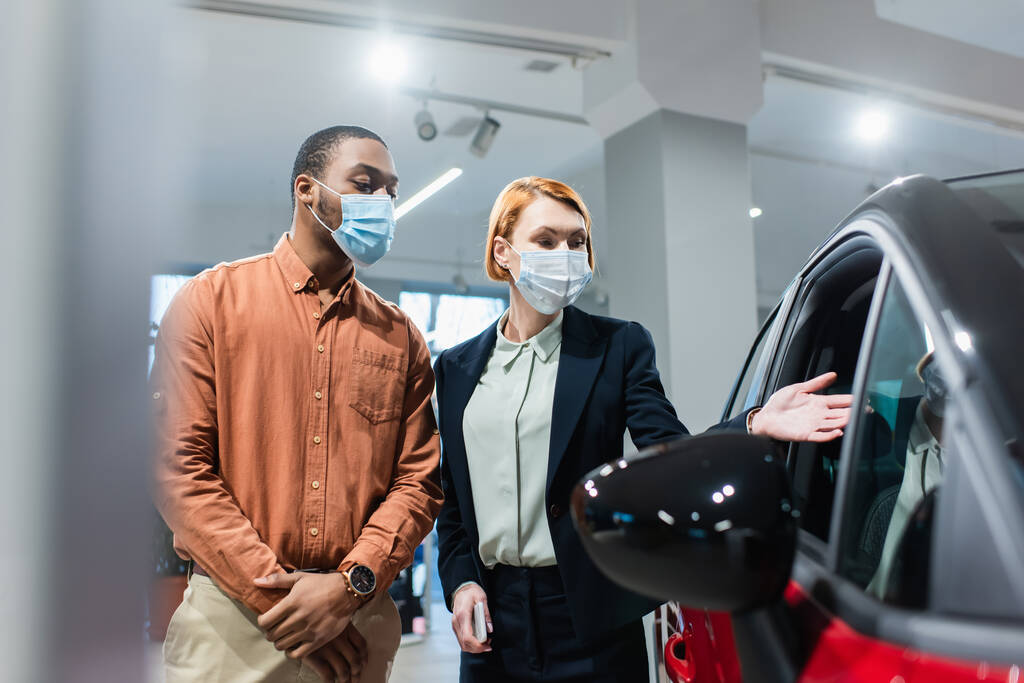 auto jälleenmyyjä lääketieteellinen naamio osoittaa autoa lähellä afrikkalainen amerikkalainen asiakas - Valokuva, kuva