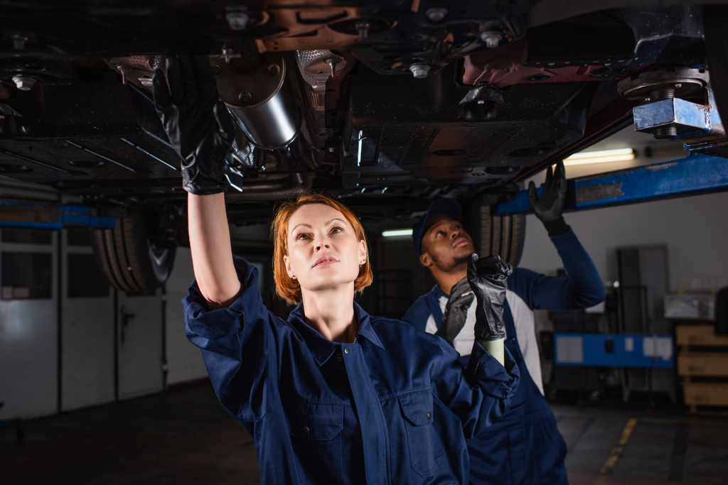 multiethnic mechanics checking bottom of lifted car in workshop - Foto, Bild