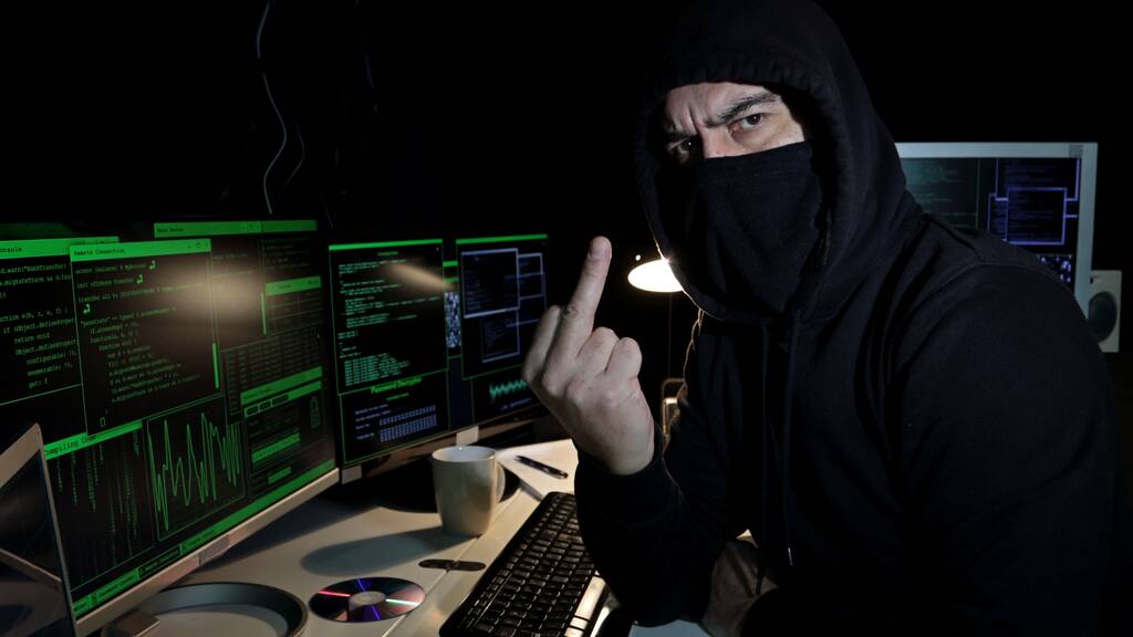 Cyber hacker with hood and covered face looks at the camera showing middle finger with serious look. Cyber attack. - Photo, Image