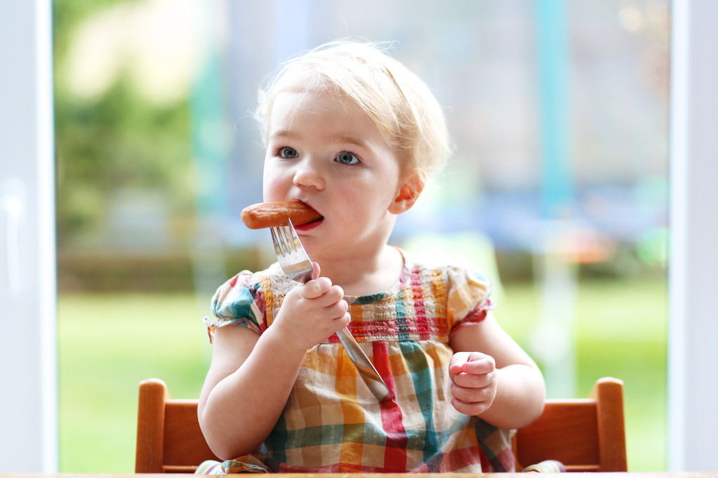 Funny little girl eating sausage from fork - Photo, Image