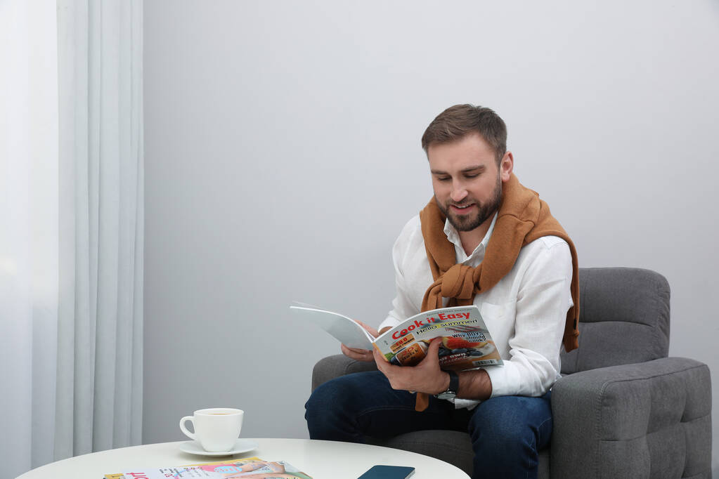 Красивий чоловік читає журнал в кріслі вдома
 - Фото, зображення