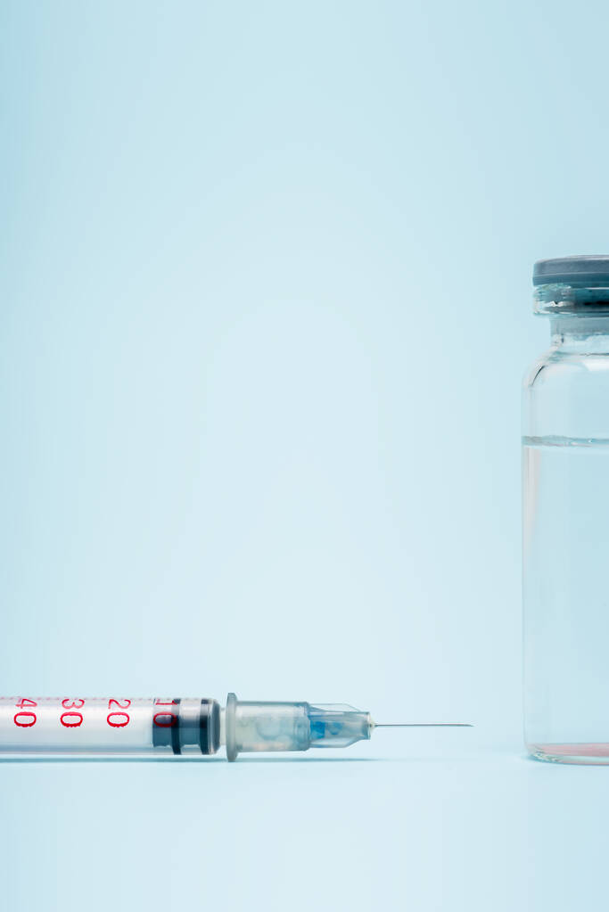青い背景に注射器の近くにあるワクチンボトルを間近に見ることができます - 写真・画像