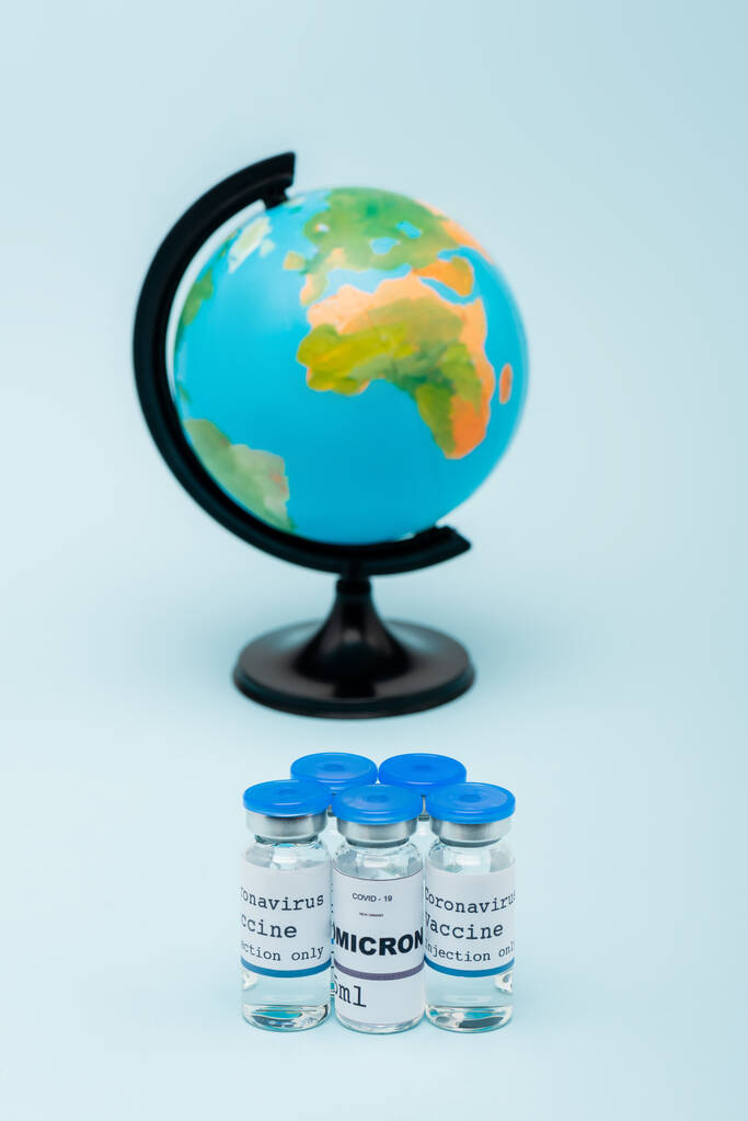 covid-19 omicron variant vaccine bottles near blurred globe on blue background - Zdjęcie, obraz