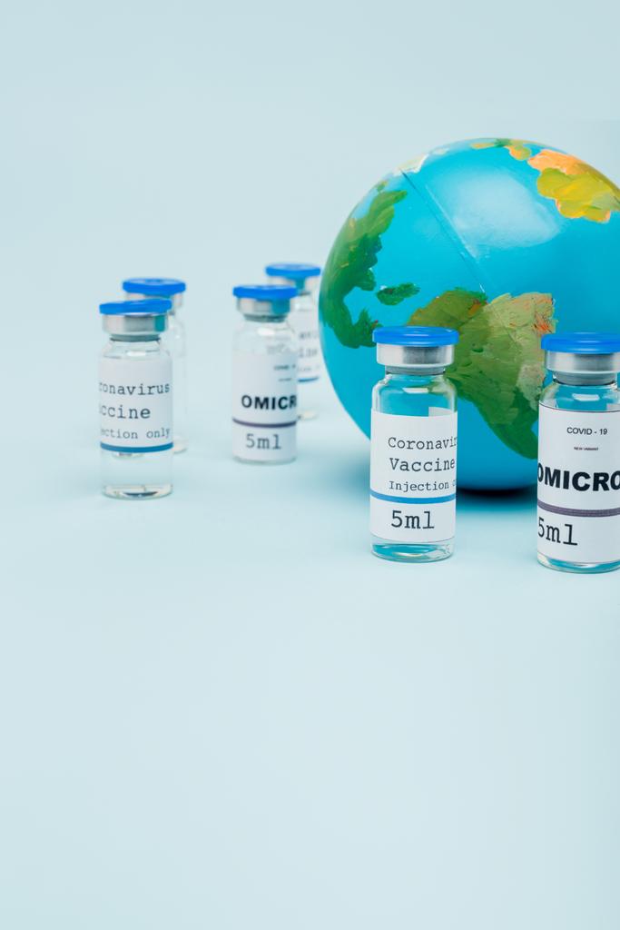 covid-19 and omicron strain vaccine jars near globe on blue - Foto, afbeelding